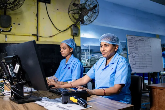 Female factory workers at desks using computers in an industrial setting, illustrating modern blue-collar employment. BI for operations management